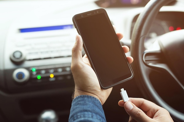車の中でモバイルスマートフォンのバッテリーを充電する男の手を接写し、画面を空白のままにしておきます