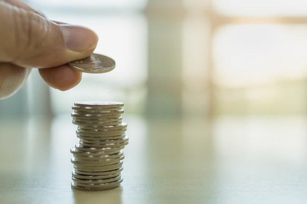 Close up of man hand holding a coin and put to top of stack of coins 