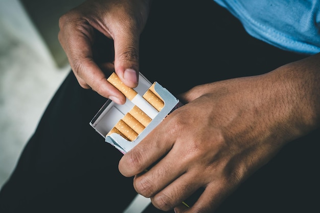 Photo close up man hand holding peel it off cigarette pack prepare smoking a cigarette packing line up