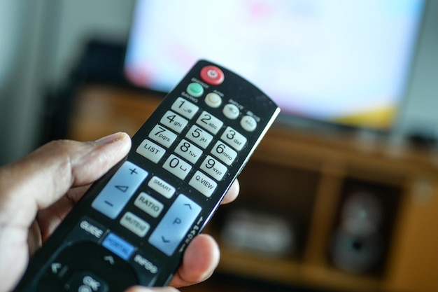 Primo piano della mano dell'uomo che tiene il telecomando della tv