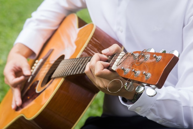 Close up of man hand playing guitar on green lawn.