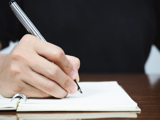 Крупным планом мужчина пишет ручку на странице дневника на столе