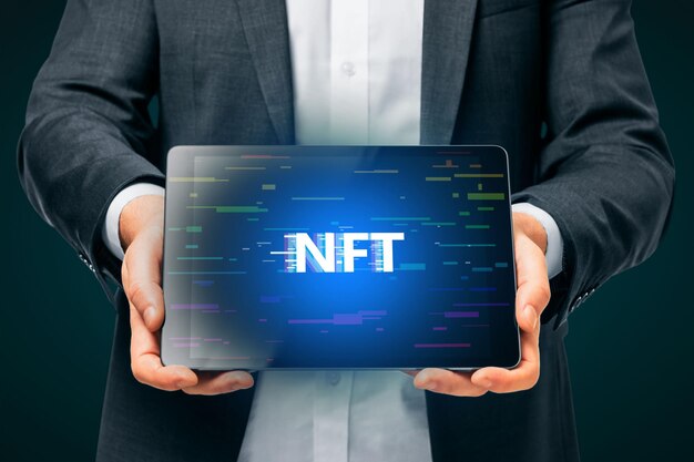 Close up of man hands holding tablet with creative glowing NFT hologram on dark background Nonfungible token and cryptocurrency concept