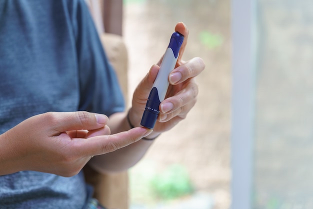 Primo piano delle mani dell'uomo utilizzando la lancetta sul dito per controllare il livello di zucchero nel sangue mediante il glucometro. utilizzare come medicina, diabete, glicemia, assistenza sanitaria e concetto di persone.