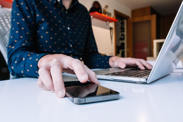 Foto primo piano delle mani dell'uomo utilizzando il computer portatile che controlla lo smartphone