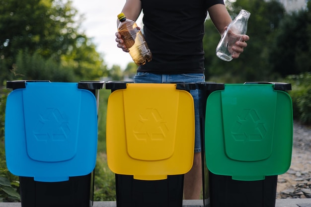 男のクローズアップは、2つの異なるボトルのプラスチックとガラスを保持し、異なるリサイクルに解凍します