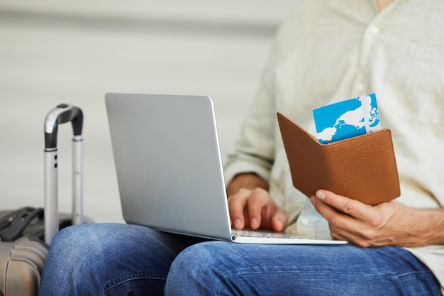 Photo close-up of man holding airplane tickets typing on laptop computer he registering the tickets online