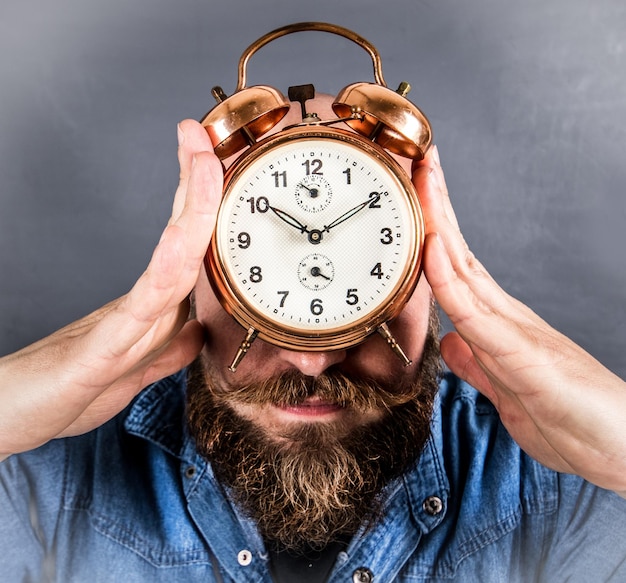 Close-up of man holding alarm clock on face