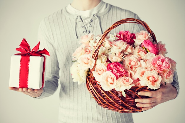 close up of man holding basket full of flowers and gift box.