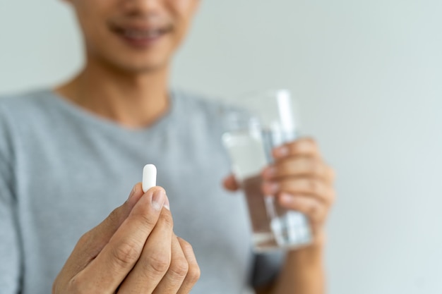 Primo piano di un uomo che tiene in mano un integratore alimentare o un farmaco e un bicchiere d'acqua pronto a prendere la medicina. concetti di salute delle persone.