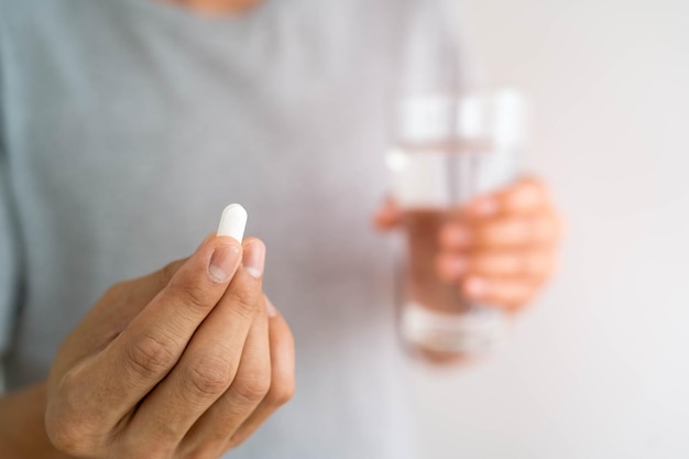 Close up of a man holding a dietary supplement or medication and a glass of water ready to take medicine health concepts of people