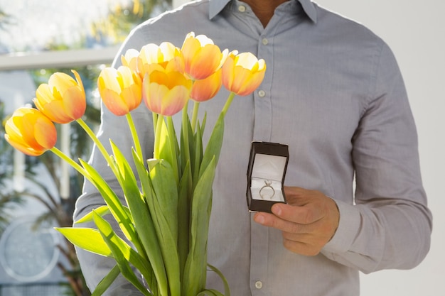 Close-up of man holding engagement ring and flower bouquet