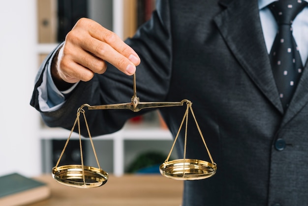 Photo close-up of man holding golden scales of justice in hand