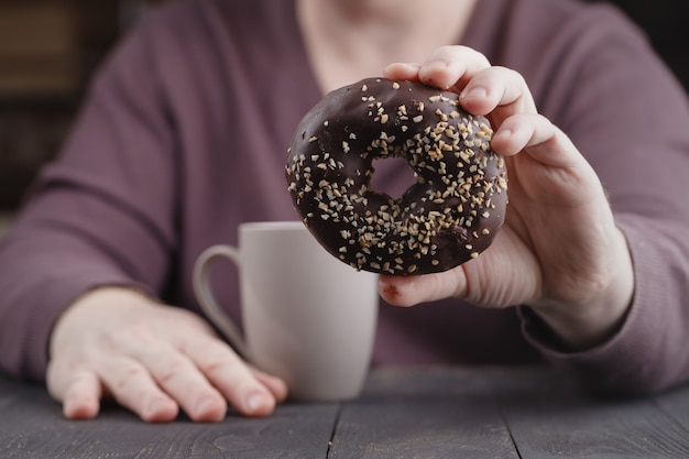 Close up of a man holding in his hands a doughnut with chocolate