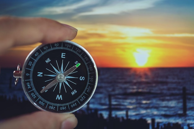 Foto close-up di un uomo che tiene una bussola di navigazione sul mare contro il cielo durante il tramonto