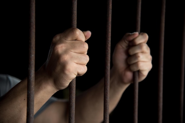 Close-up of man holding prison bars