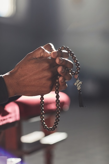 Close-up of man holding rosary beads praying while visiting the church