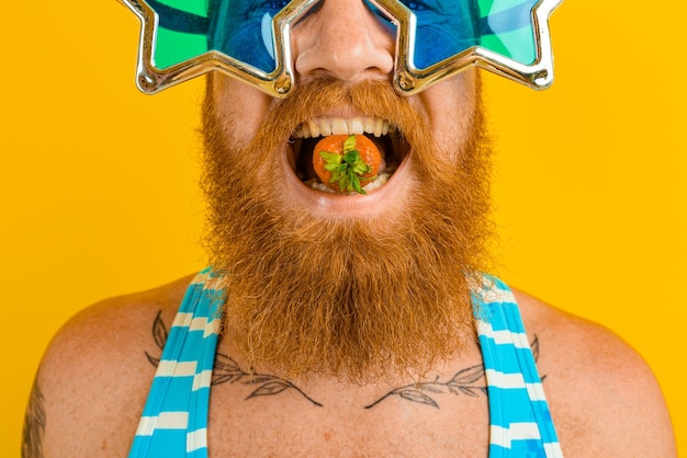 Photo close-up of man holding strawberry in mouth against yellow background