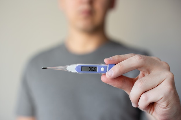 Close up of man holding thermometer in his hands, temperature is 36.6 degrees Celsius