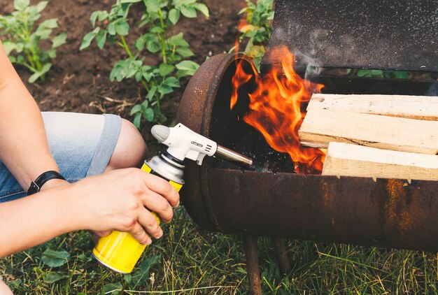 Photo close up man holds a gas burner with a balloon and makes a fire in the grill flame gun on the