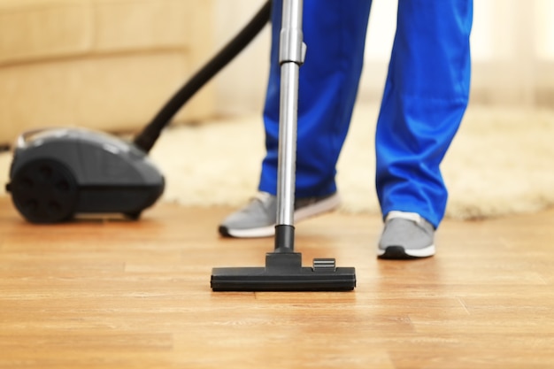 Photo close up of man hoovering floor with vacuum cleaner