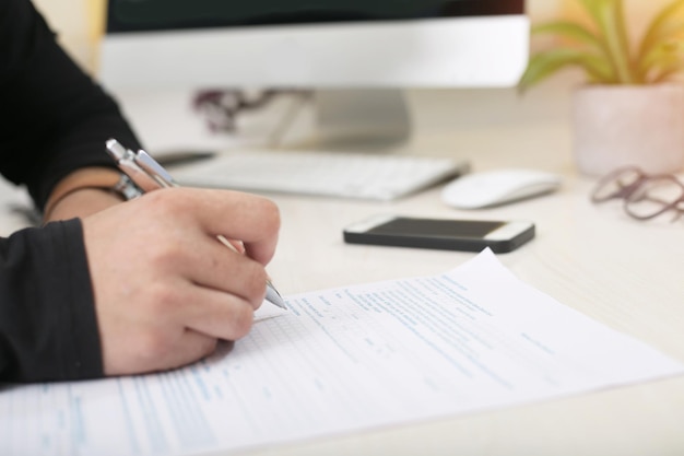 Close up of man is holding pen in hand and filling form on desk