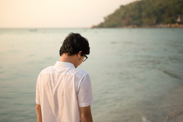 close-up man is standing on the beach with wave from sea on his traveling tip