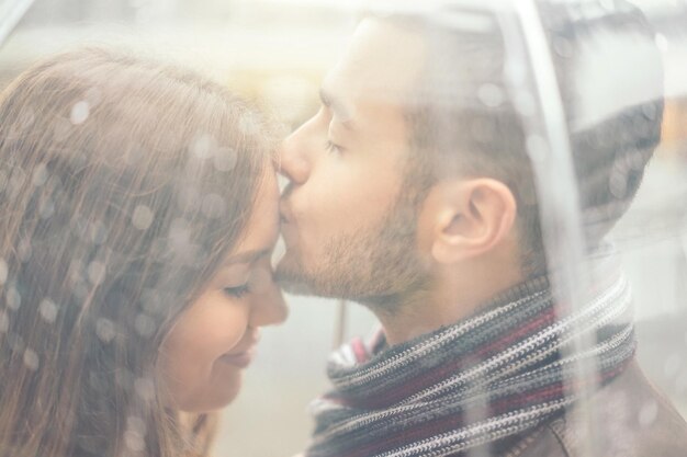 Photo close-up of man kissing on woman forehead seen through umbrella