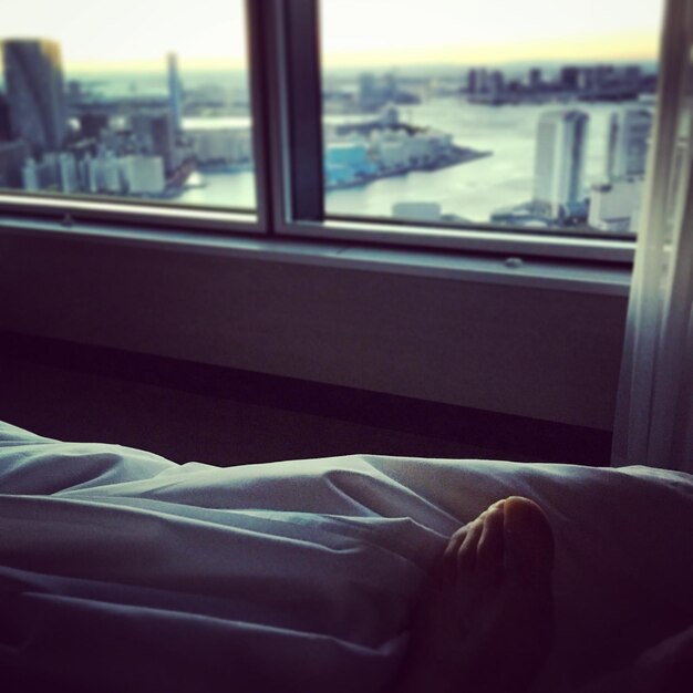 Close-up of man leg on bed with city seen through window