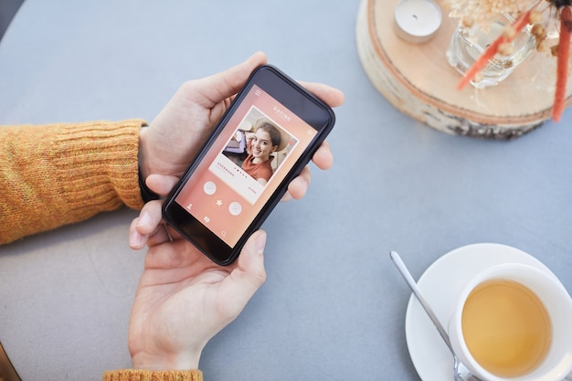 Close-up of man looking at photo of beautiful girl while using online dating app on his mobile phone