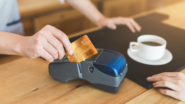 Close up of man paying with credit card in cafe for coffee in morning lights