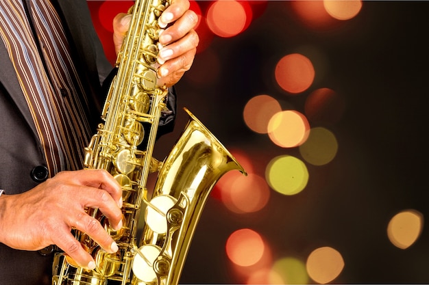 Close-up man playing on saxophone on blurred golden background