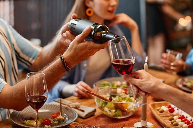 Primo piano dell'uomo che versa il vino nel bicchiere durante la cena con un ambiente caldo e accogliente