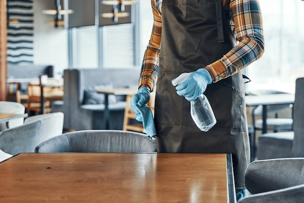 Foto primo piano di un uomo in guanti protettivi che pulisce il tavolo per i clienti mentre prepara il ristorante per l'apertura durante la pandemia