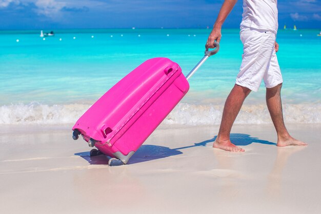 Close up a man pulls luggage on white sand