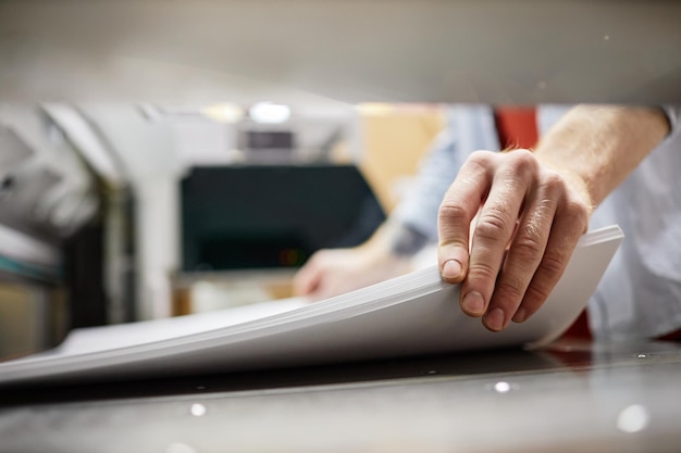 Close up of man putting stack of paper in printing machine at publishing shop copy space