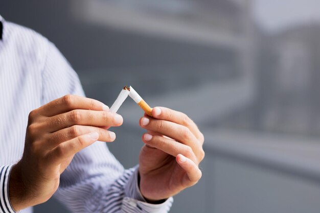 Close-up of man quitting smoking and breaking a cigarette copy space