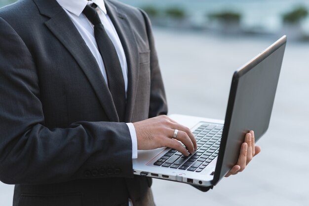 Close-up of a man's hand in a business suit. Prints on a laptop keyboard while standing 