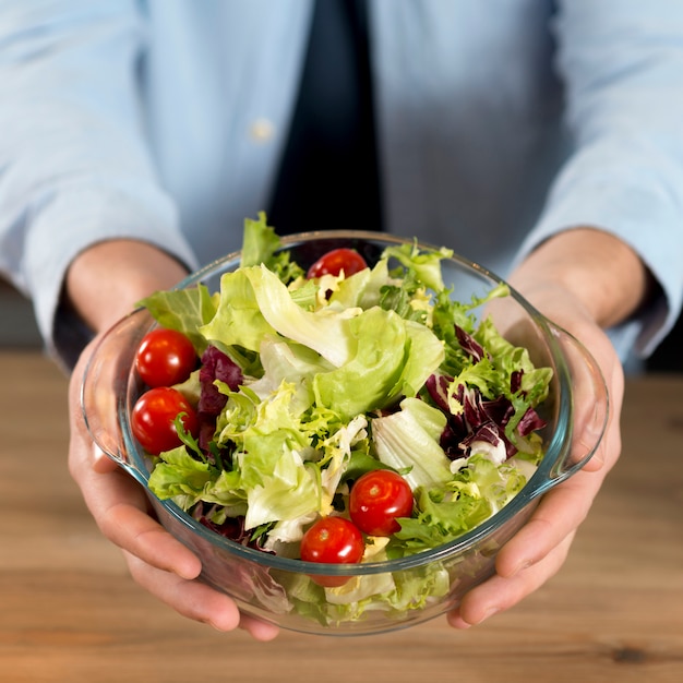 Primo piano della mano di un uomo che tiene ciotola di insalata fresca sopra la scrivania in legno