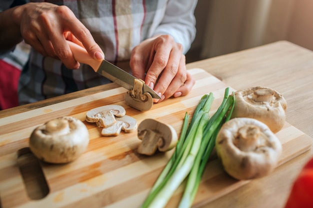 Close up of man's hand holding knife and cutting mushrooms