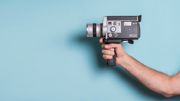 Крупный план мужской руки, держащей старомодную видеокамеру на синем фоне