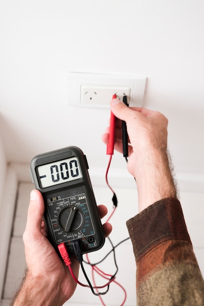 Close-up of man's hand plugging digital multimeter in plug at home