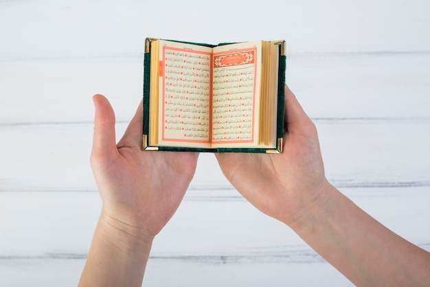 Photo close-up of a man's hand reading quran over the white wooden table