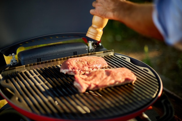 屋外のバーベキューグリルのガスグリルで肉を味付けする男の手のクローズアップ