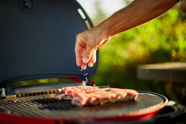 屋外のバーベキューグリルのガスグリルで肉を味付けする男の手のクローズアップ