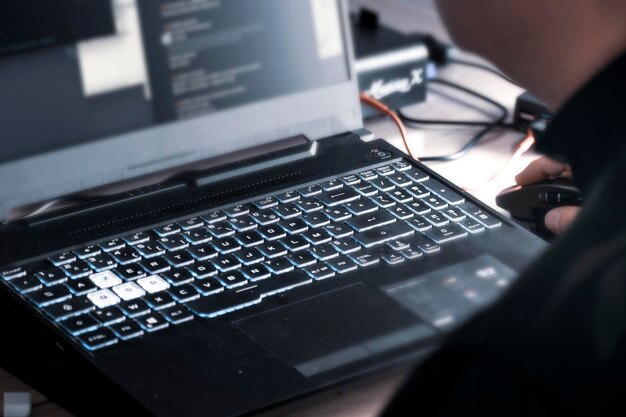 Photo close up of man's hand using wireless mouse and laptop computer with blue backlit keyboard