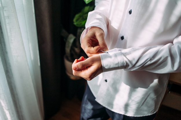 close up of man in shirt dressing up and adjusting tie on neck at home.