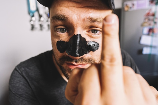 close up of man showing middle finger hand sign and black Mask Peeling cosmetic - gesture, morals and people concept