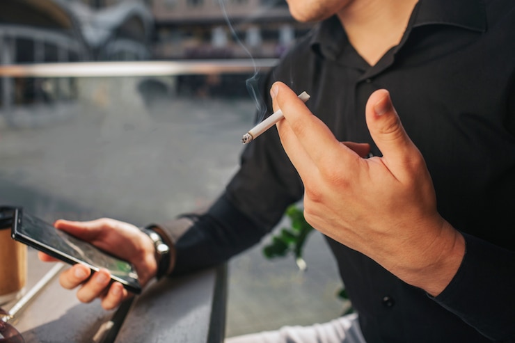 Photo 座っていると携帯電話とタバコを保持している男のクローズアップ。男の煙。彼は電話を見ます。