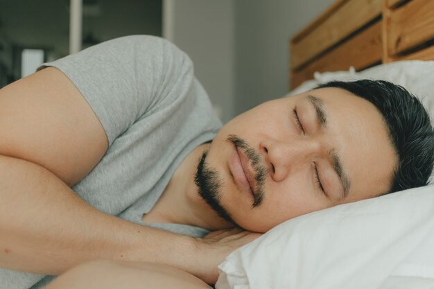 Chiuda sull'uomo che dorme sul suo letto con la faccia felice. concetto di buon sonno.